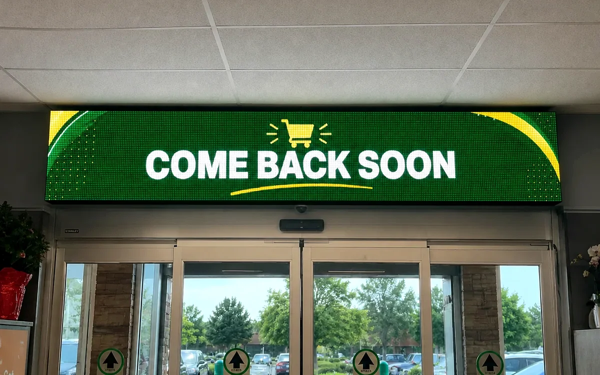 Wide green LED banner reading Come Back Soon above a supermarket's automatic exit doors